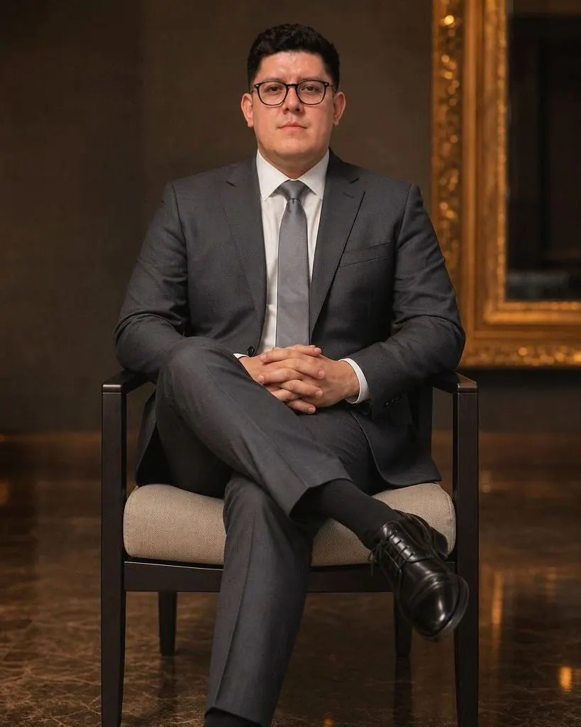 Carlos Rocha sentado en un sillón, de traje gris y corbata, en un ambiente de tonos cálidos